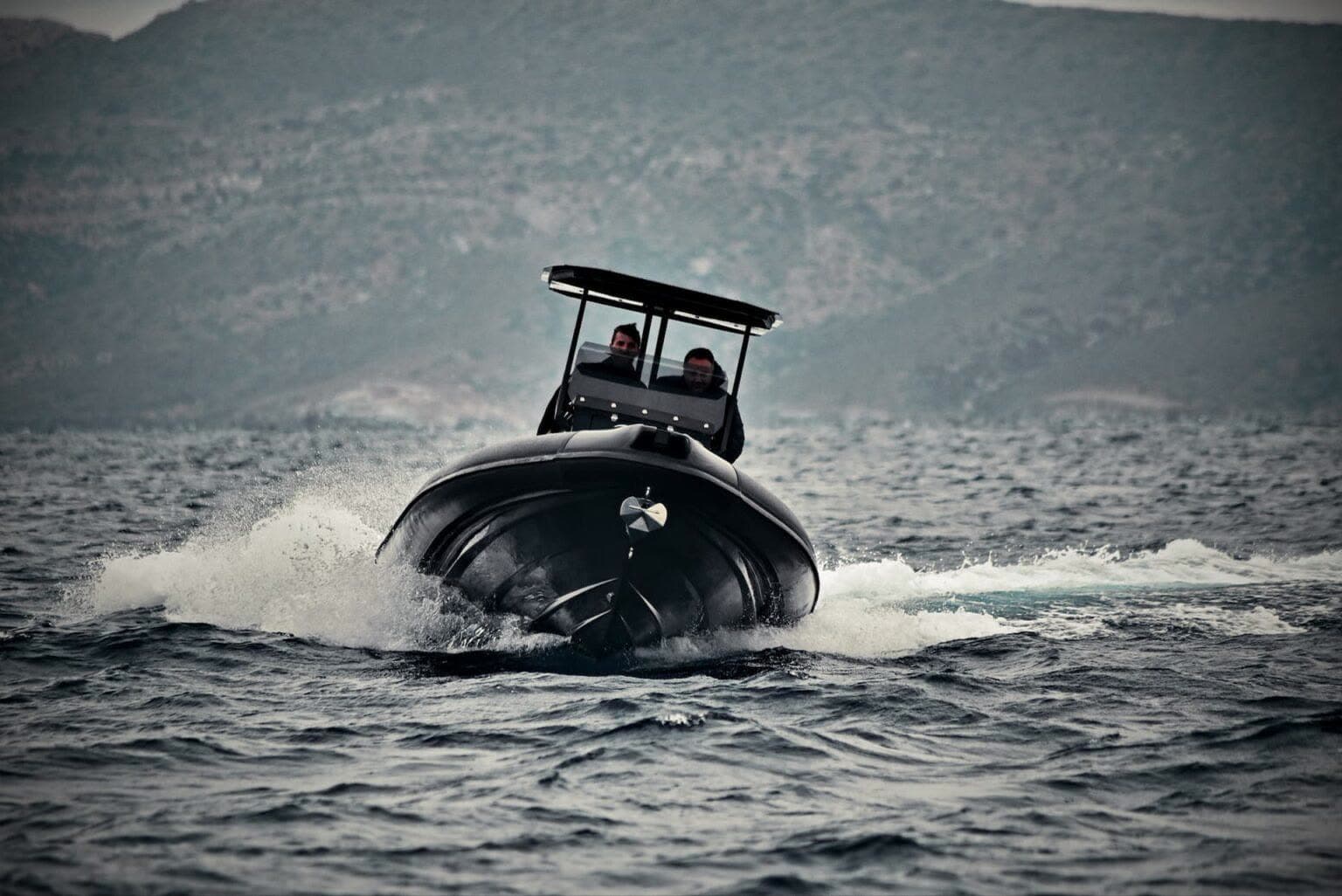 Dark Hydrohulls RIB charging toward the camera through spray